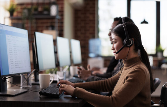 Paralyzed asian employee working at call center reception in disability friendly office. Female operator wheelchair user with impairment giving assistance on customer service helpline.